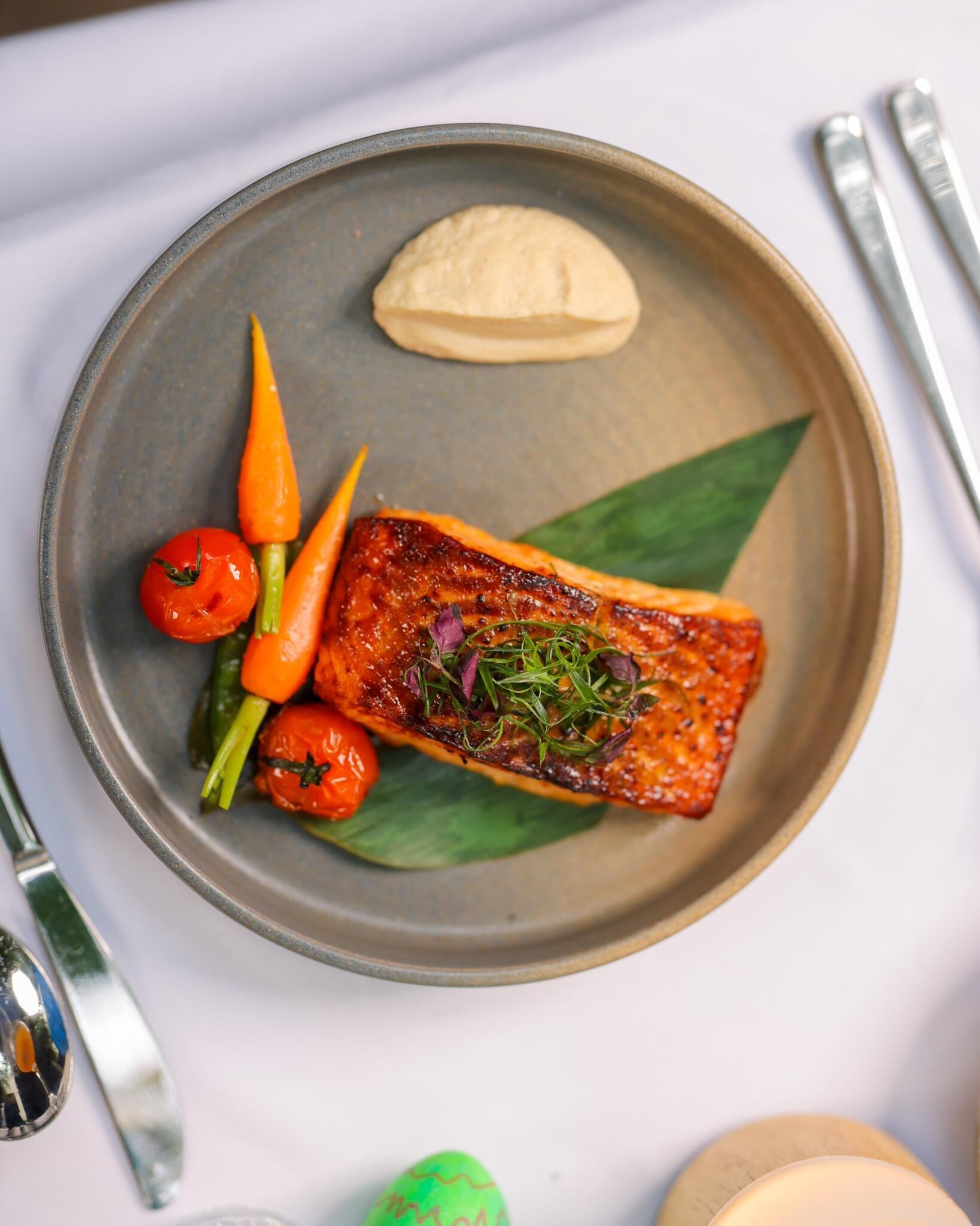 Un plato con un trozo de salmón, tomates cherry y una cucharada de salsa.