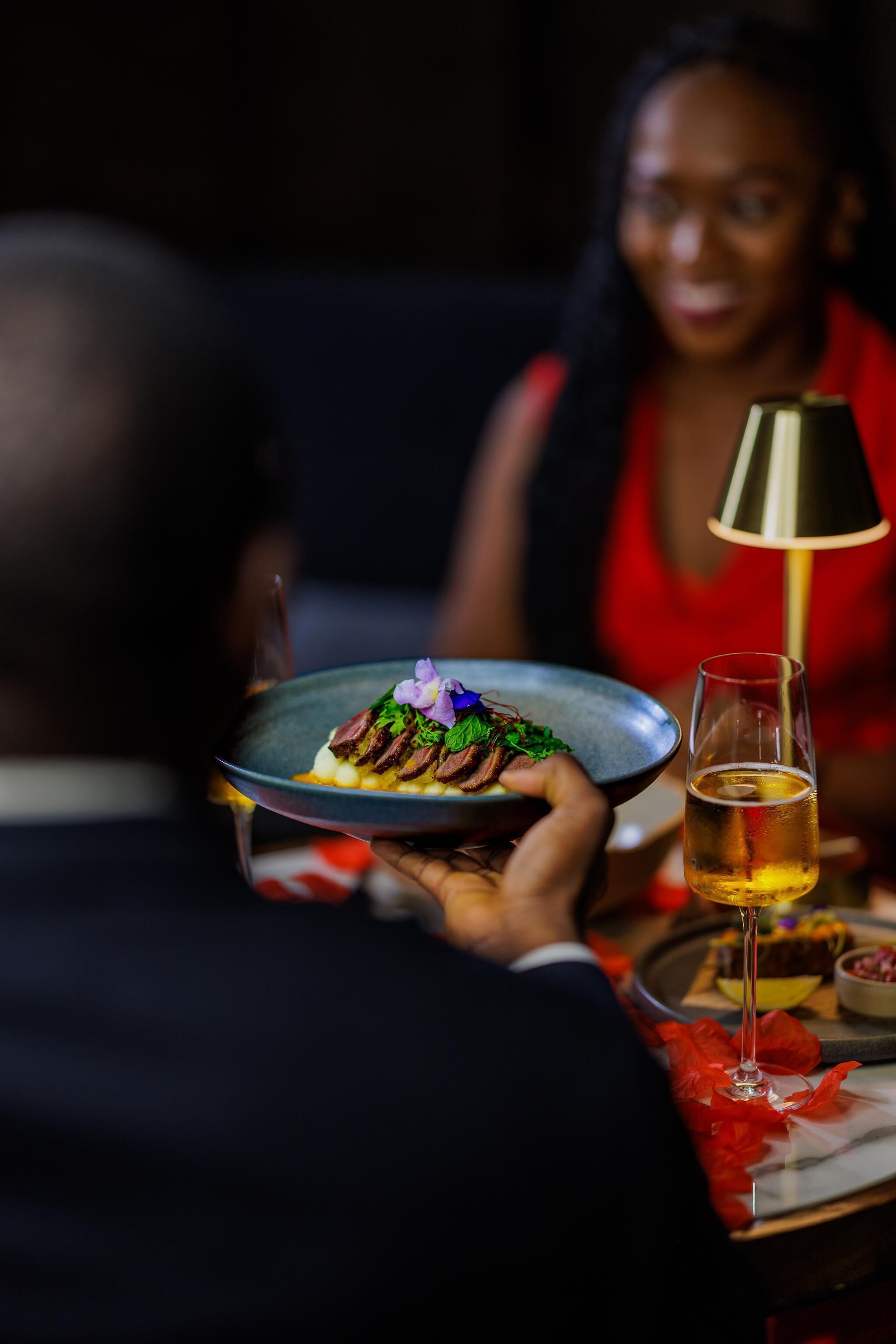 A person holding a plate with food and a glass of drink at a table.