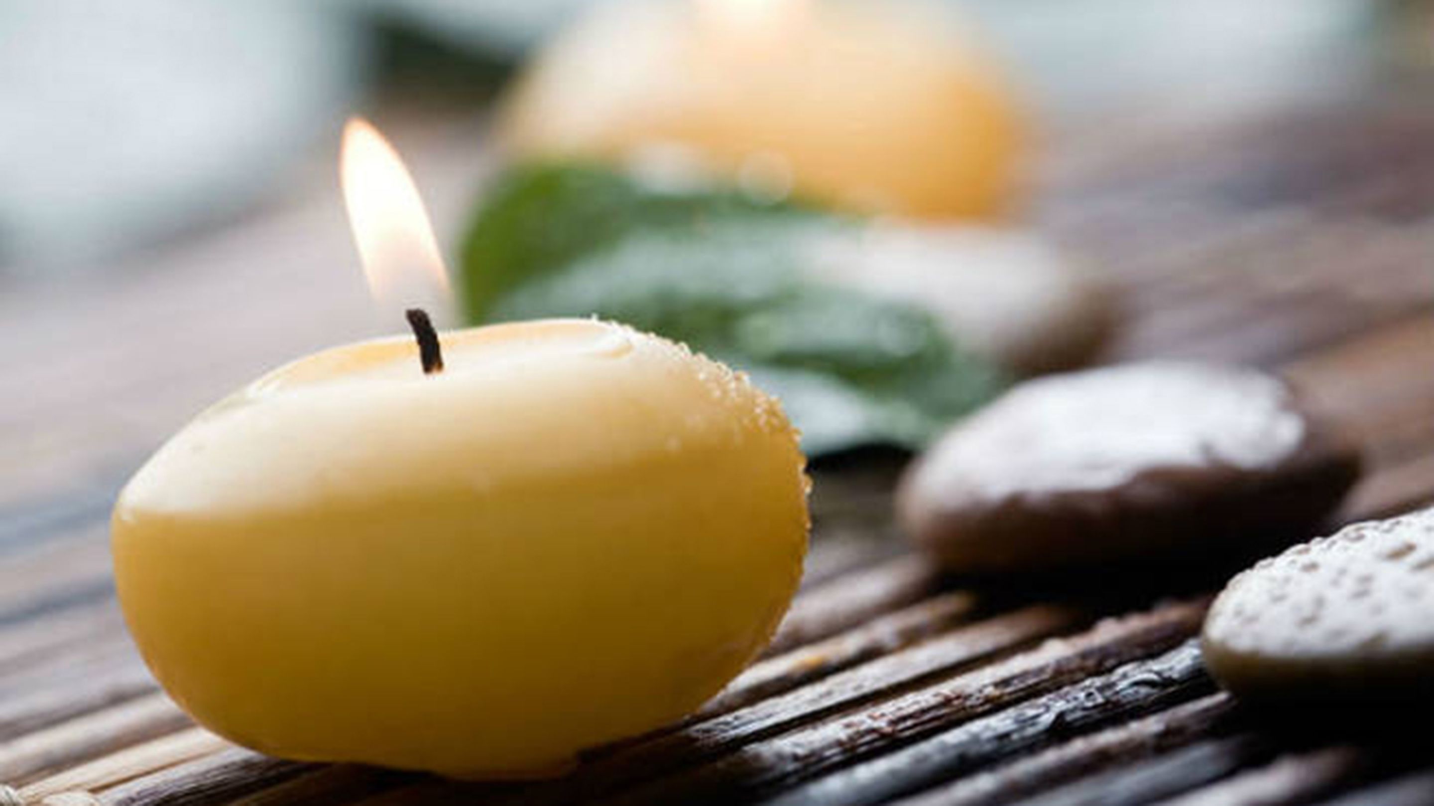 A candle on a wooden surface with stones and a green leaf.