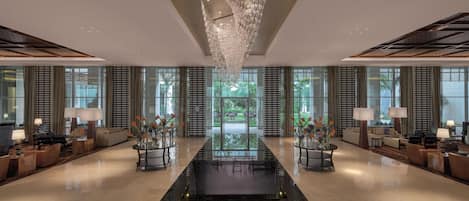 A spacious lobby with a reflective floor, a central table with vases, and a chandelier.