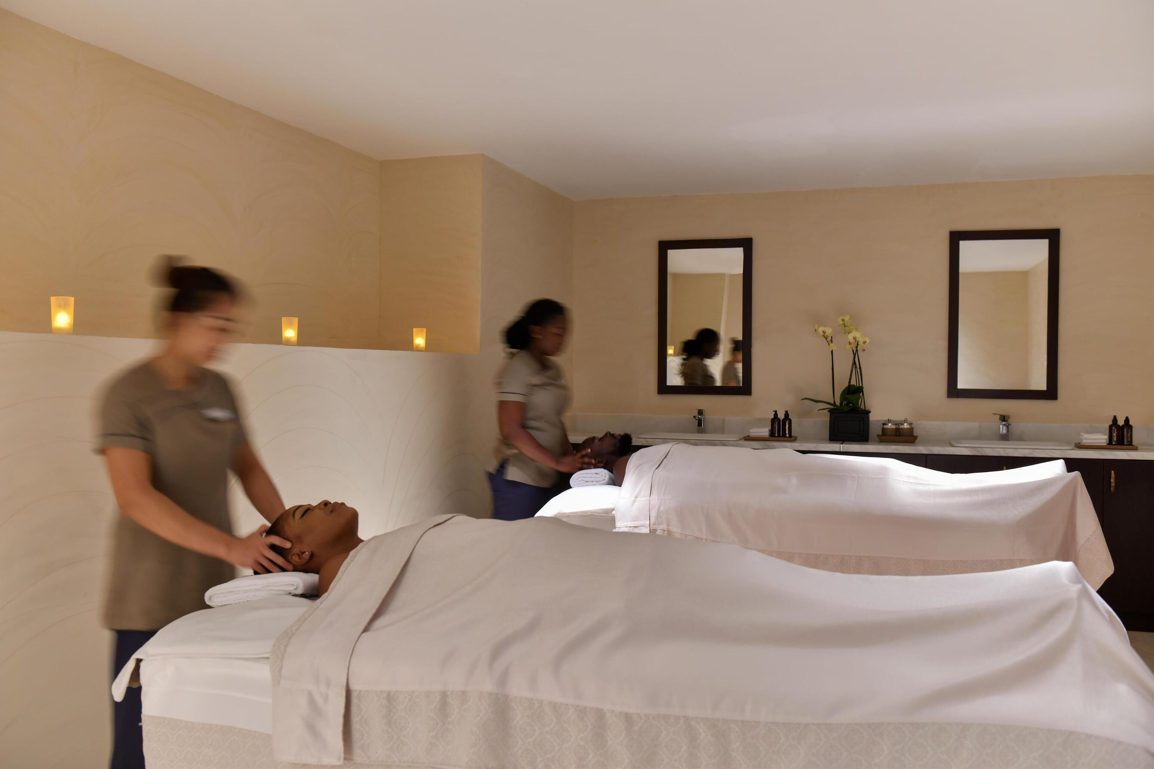 A spa room with two massage tables, a sink, and mirrors.