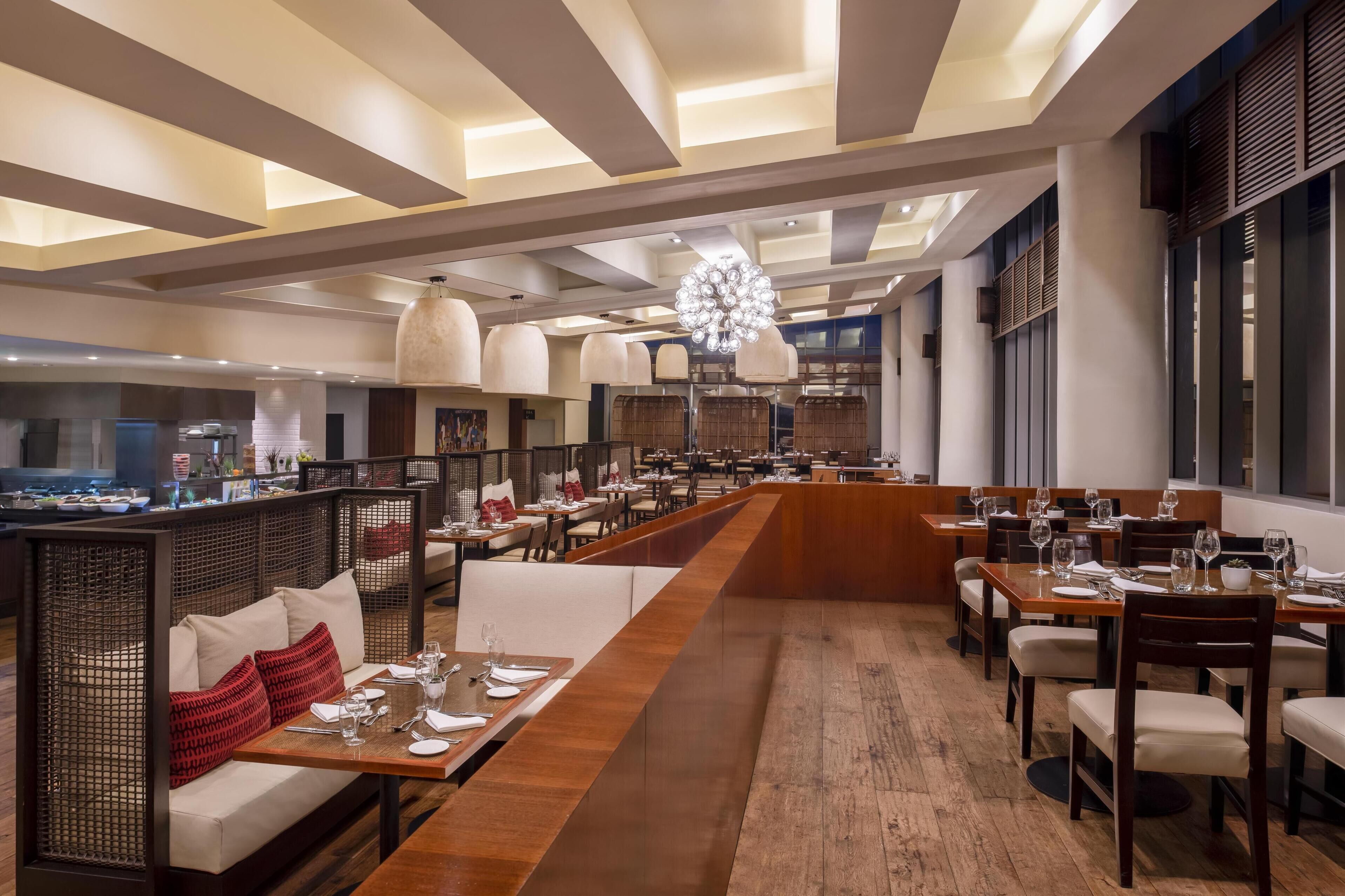 Un restaurant spacieux avec de longues tables communes, de hauts plafonds dotés d’un éclairage encastré et un lustre central.