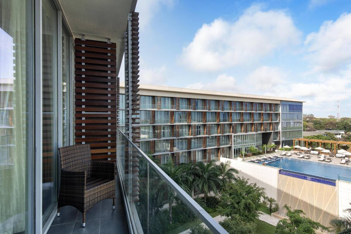 Ein modernes Hotel mit Glasbalkon, Poolanlage und üppiger Bepflanzung.