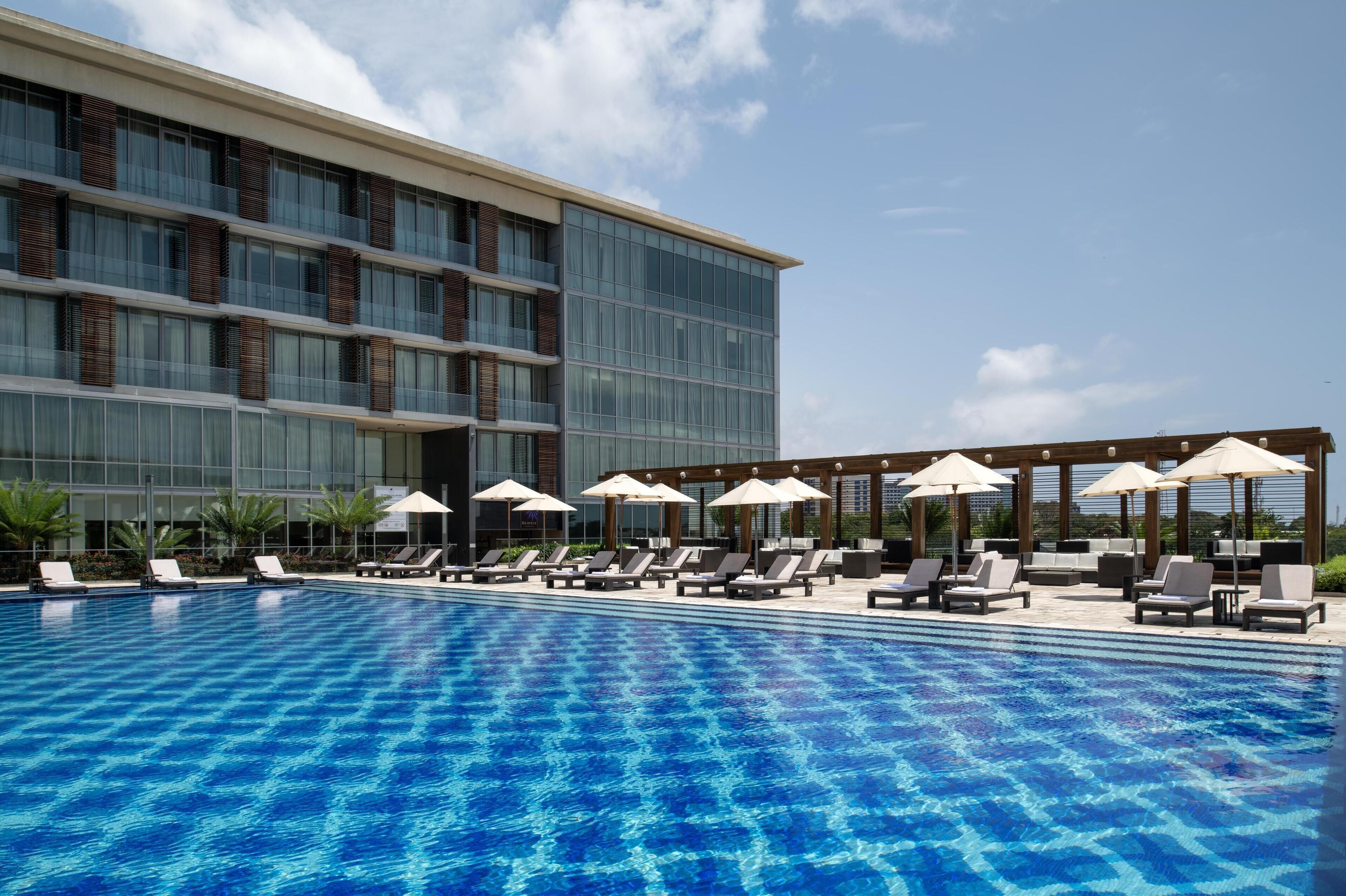A swimming pool with lounge chairs and umbrellas, surrounded by a modern building with large windows.