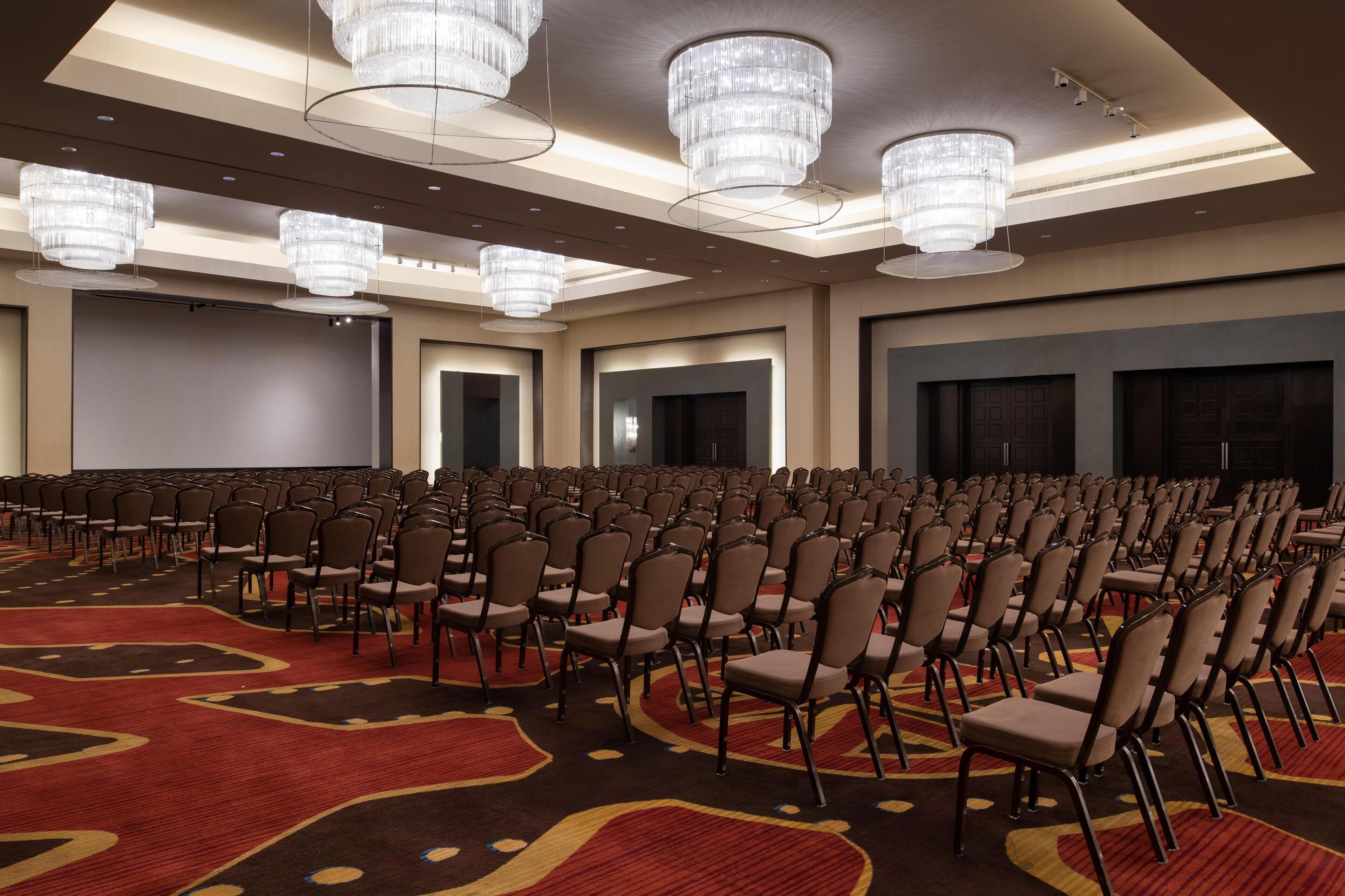 A large conference room with rows of chairs, a carpeted floor, and multiple chandeliers.