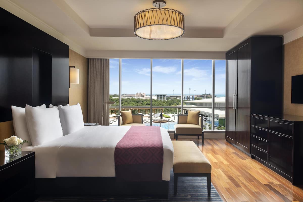 Ein Hotelzimmer mit einem großen Bett, einem Schreibtisch, einem Stuhl, einem Fernseher und Blick auf die Stadt.