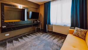 A hotel room with a large bed, a TV, a desk, and a sofa.