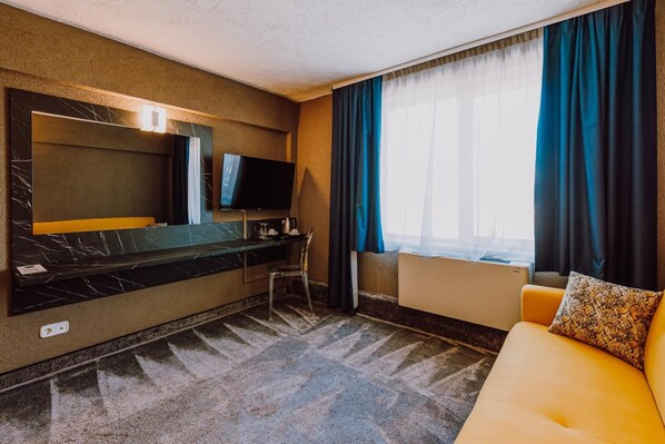 Hotellihuone, jossa on suuri sänky, televisio, työpöytä ja sohva.