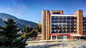 A multi-story hotel with a central courtyard, surrounded by trees and a mountain backdrop. - Park Hotel (Dolny Kubin)