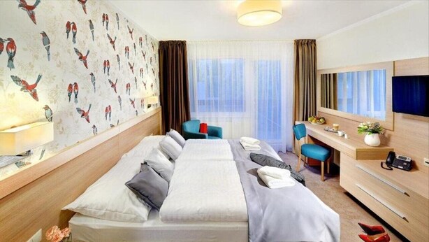 A hotel room with a large bed, a desk with a chair, a TV, and a window with curtains. - Park Hotel (Dolny Kubin)