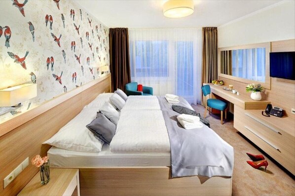 A hotel room with a large bed, a desk with a chair, a TV, and a window with curtains. - Park Hotel (Dolny Kubin)