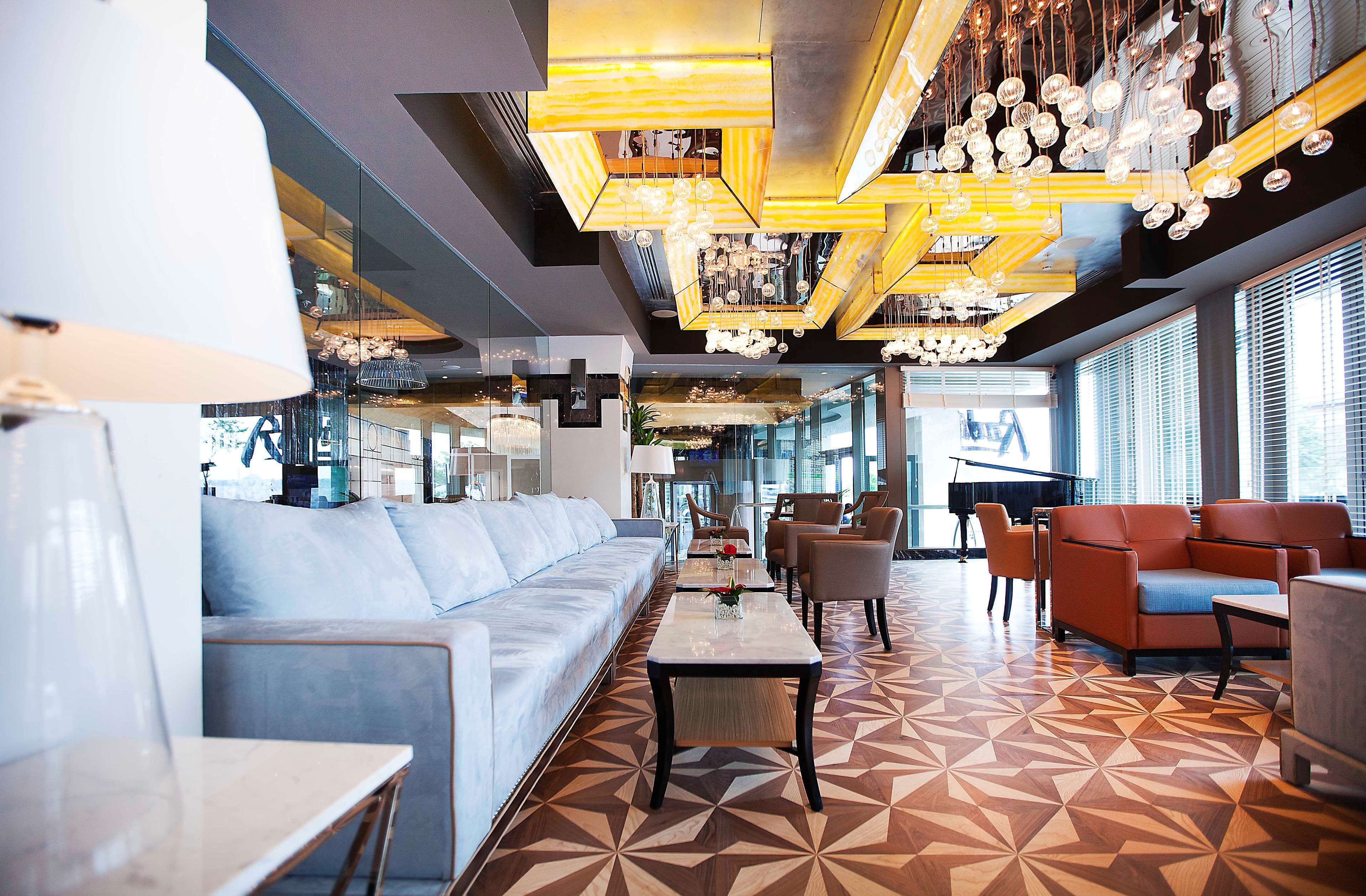 A modern lobby with a geometric patterned floor, a long sofa, and a piano in the background.