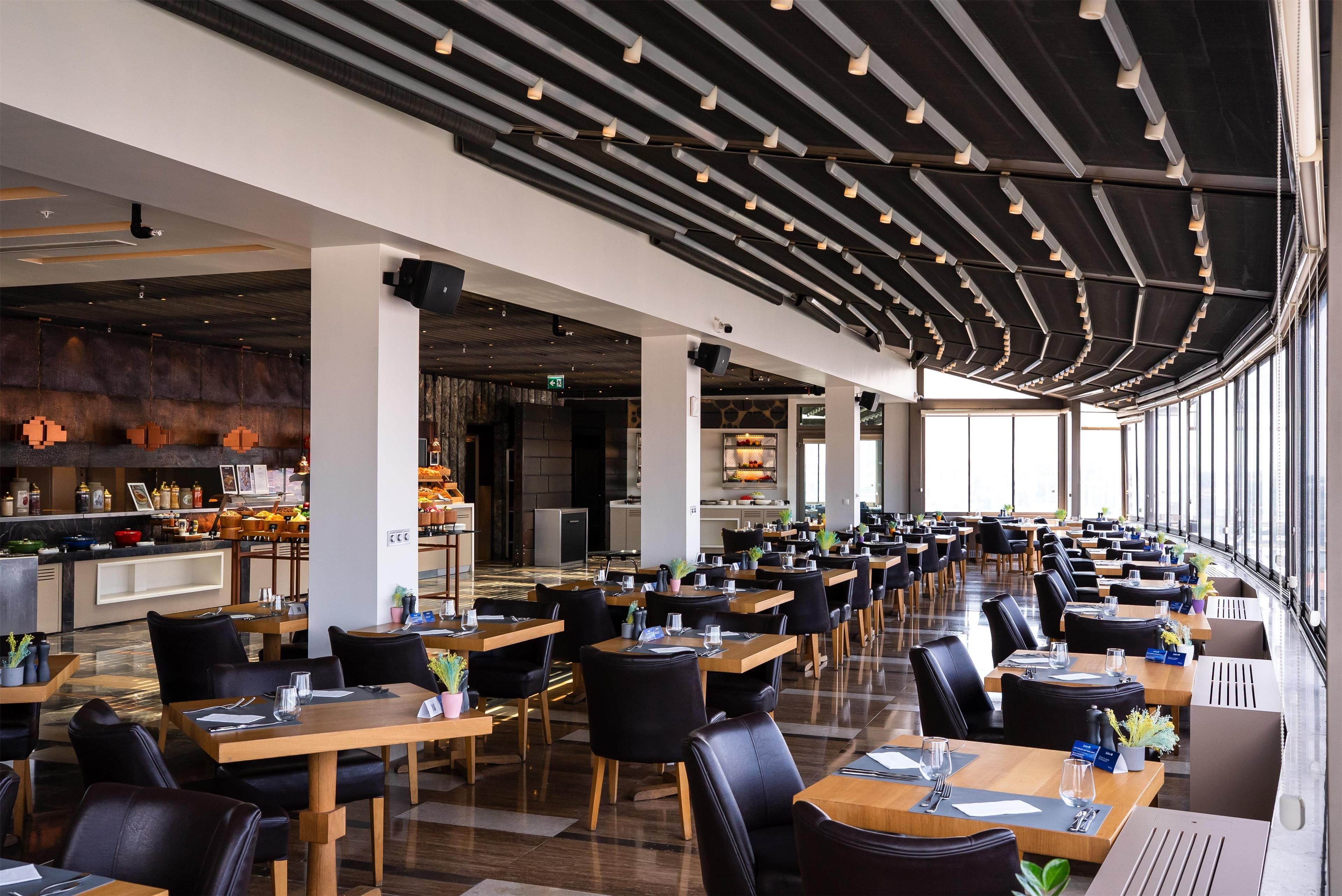 A spacious restaurant with long tables and chairs, a bar area, and large windows allowing natural light.
