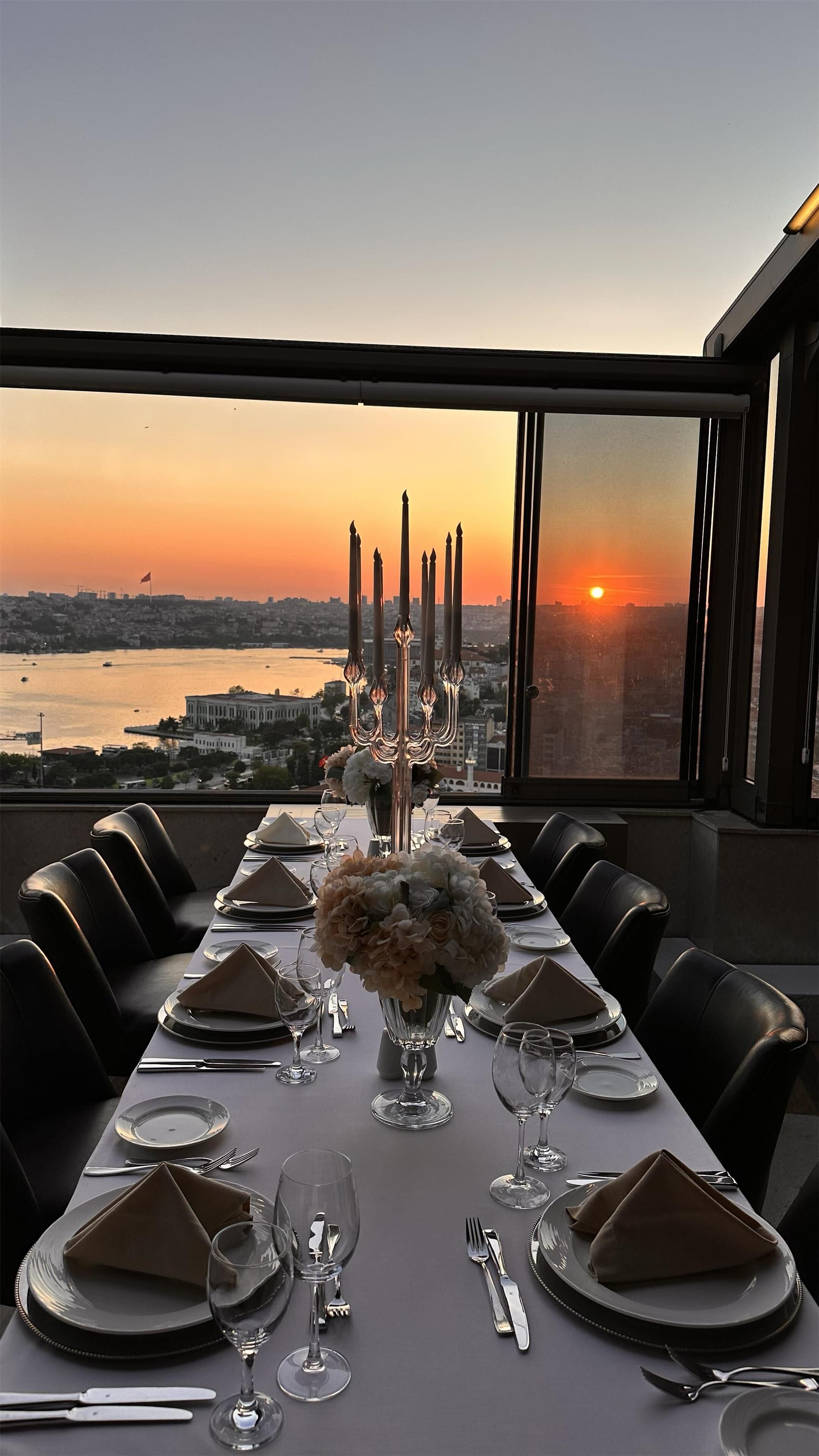 A dining table set for six with a view of a sunset over a cityscape.