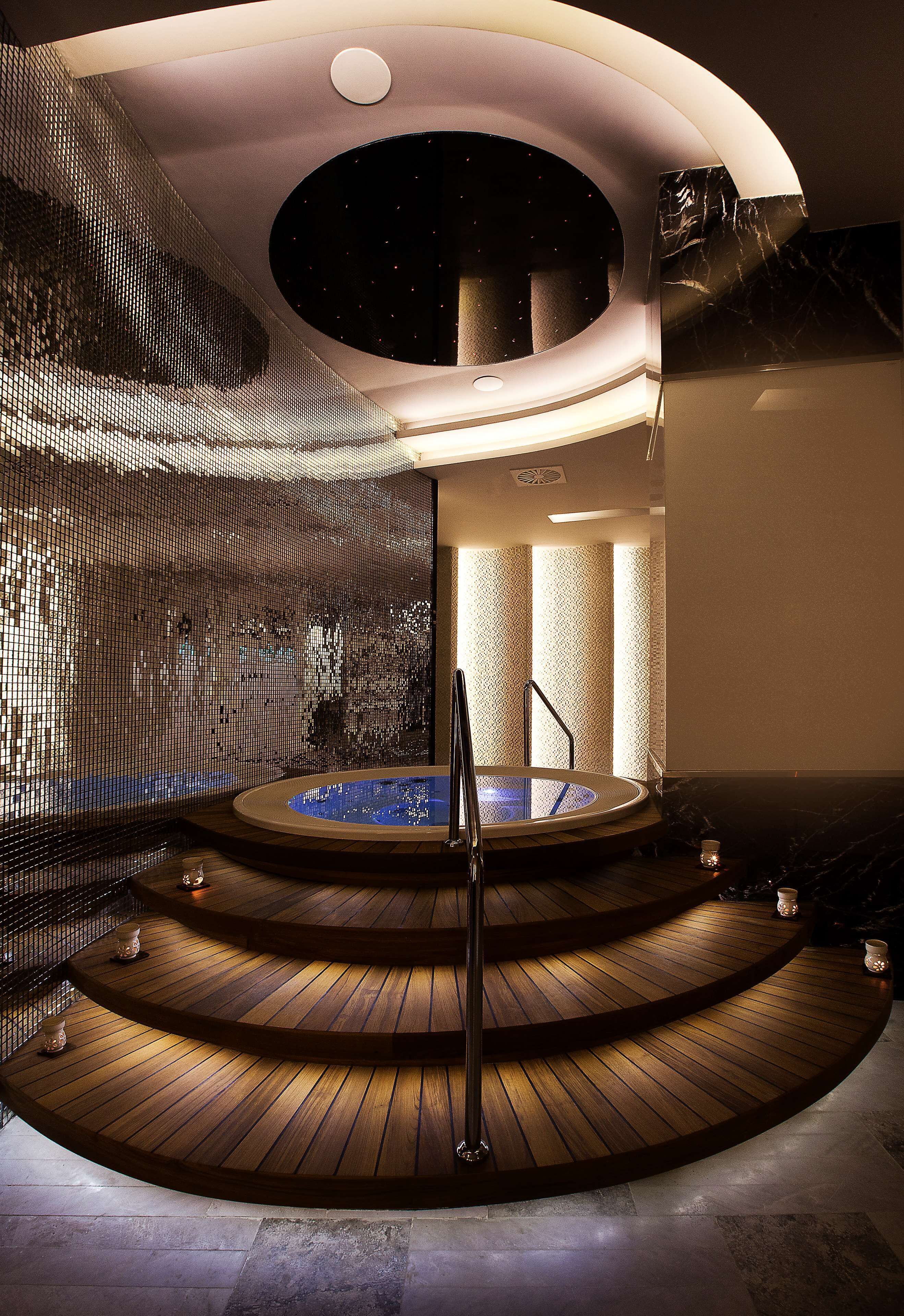 Een wellnessruimte met een rond houten platform, een bubbelbad en een mozaïekwand.