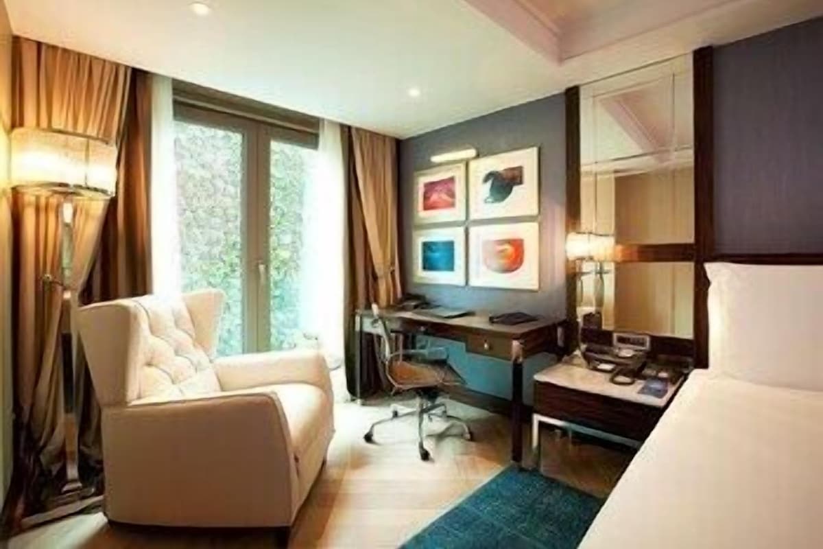 Une chambre d’hôtel avec un lit, un bureau, une chaise et une fenêtre avec des rideaux.