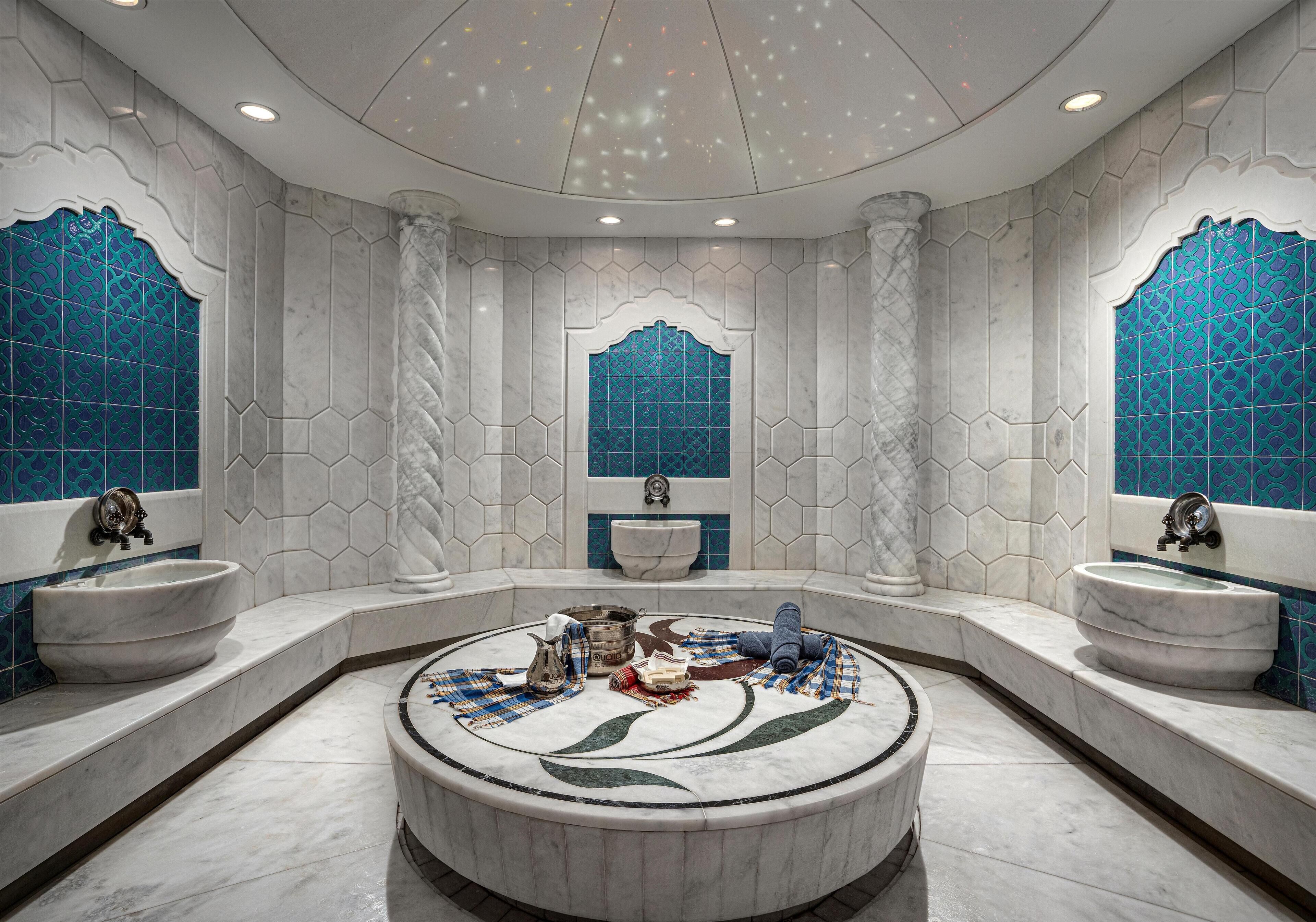 A luxurious bathroom with a central round sink, two side sinks, a large bathtub, and decorative tiles.