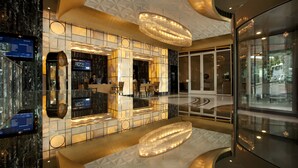 Un hall d’entrée moderne avec un mur orné de motifs géométriques, un grand lustre circulaire et une entrée en verre.