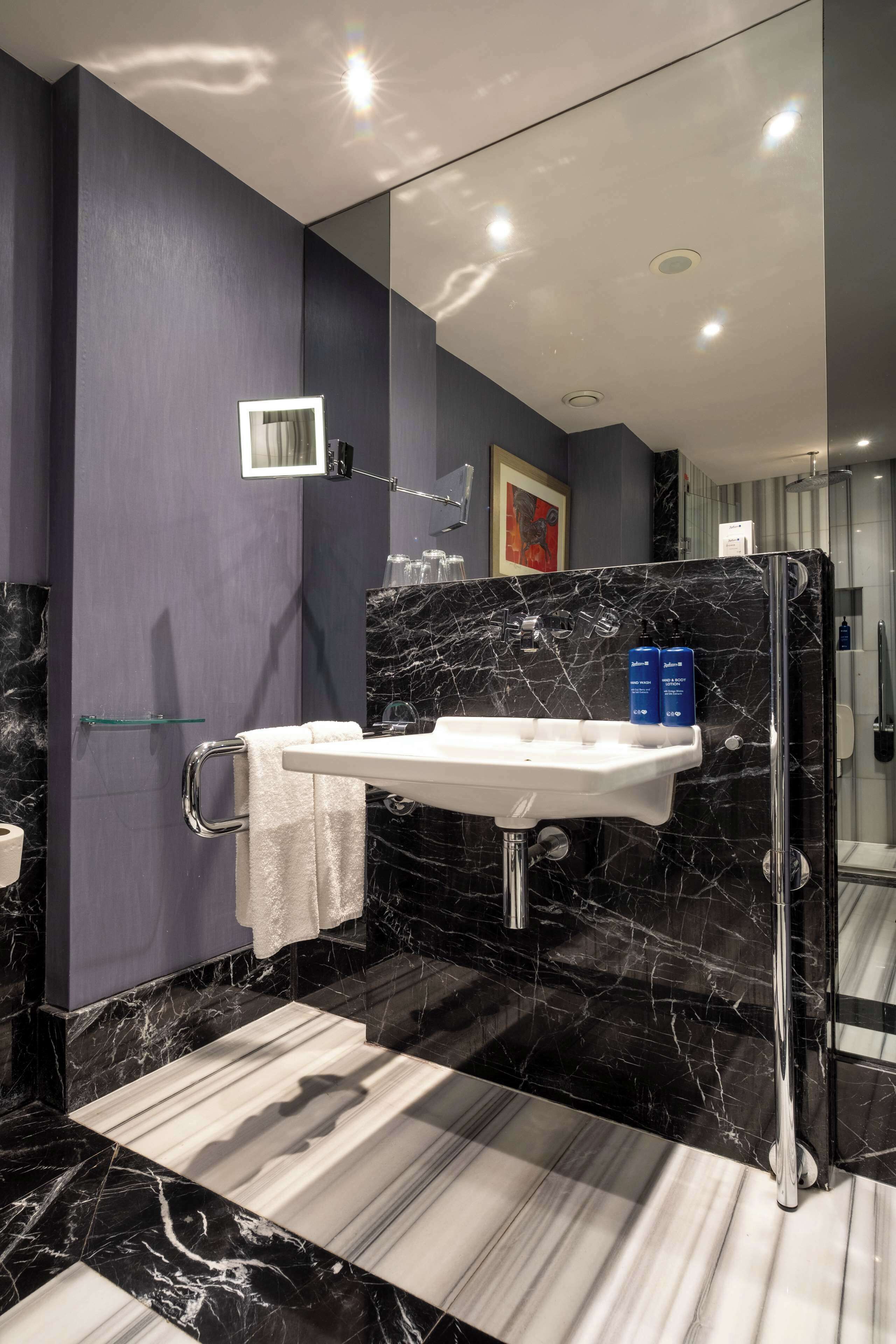 A modern bathroom with a marble sink, a glass shower enclosure, and a towel rack.