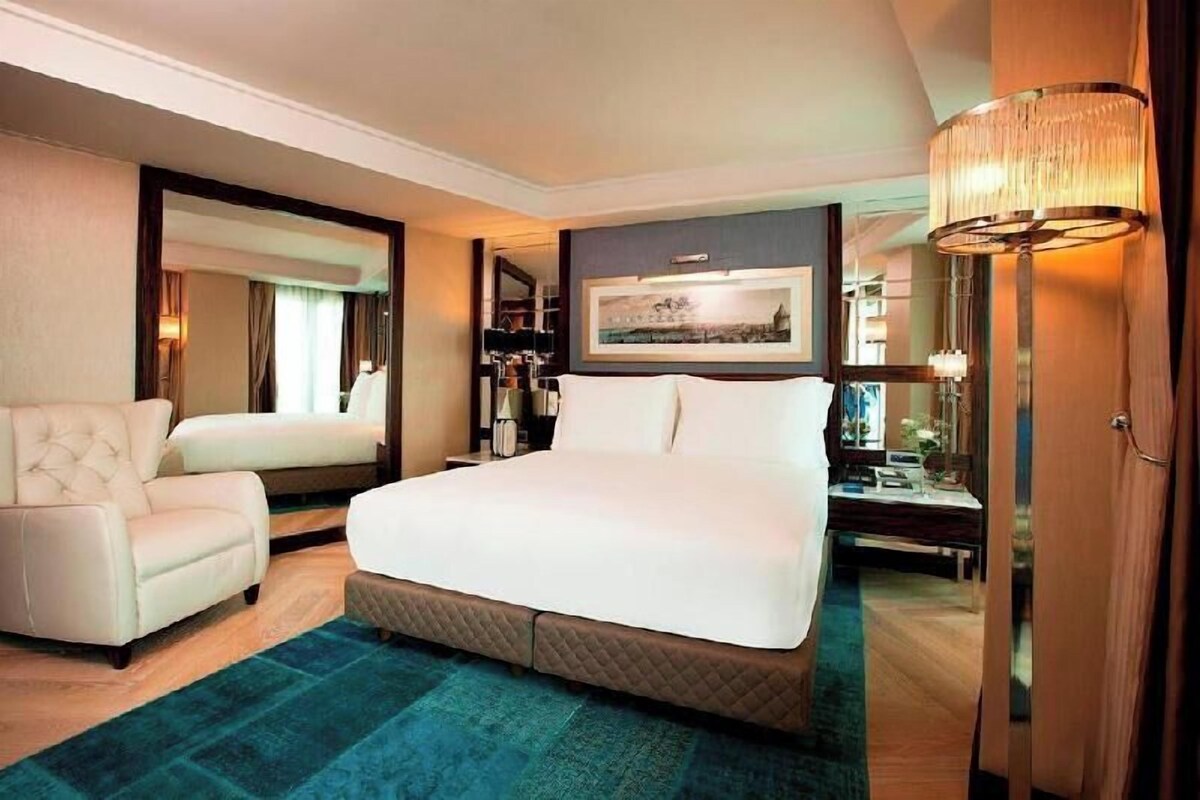 Une chambre d’hôtel dotée d’un grand lit, d’un coin salon avec un fauteuil, d’un bureau et d’une armoire.