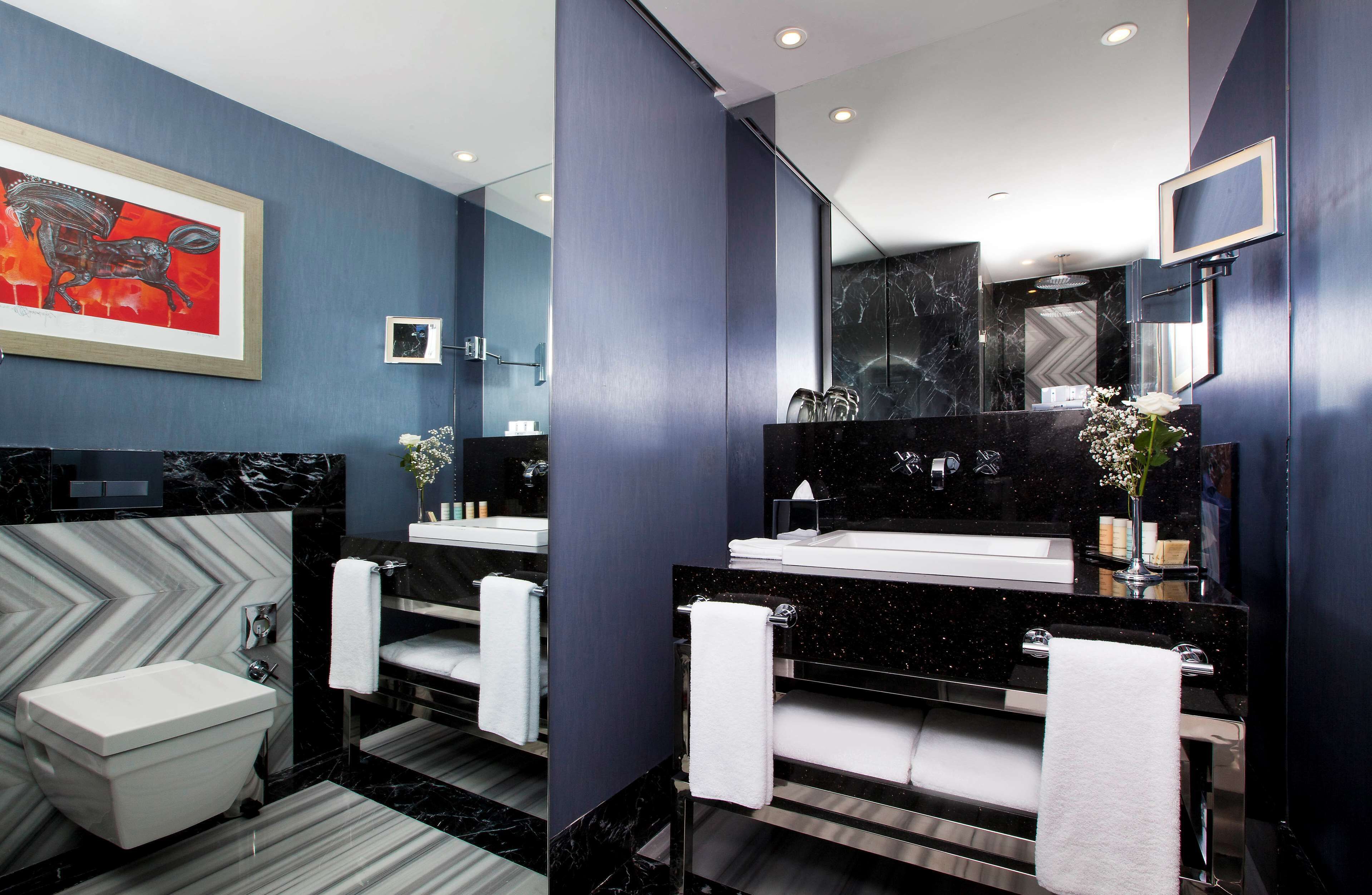 A modern bathroom with a large mirror, two sinks, a bathtub, and a decorative horse painting on the wall.
