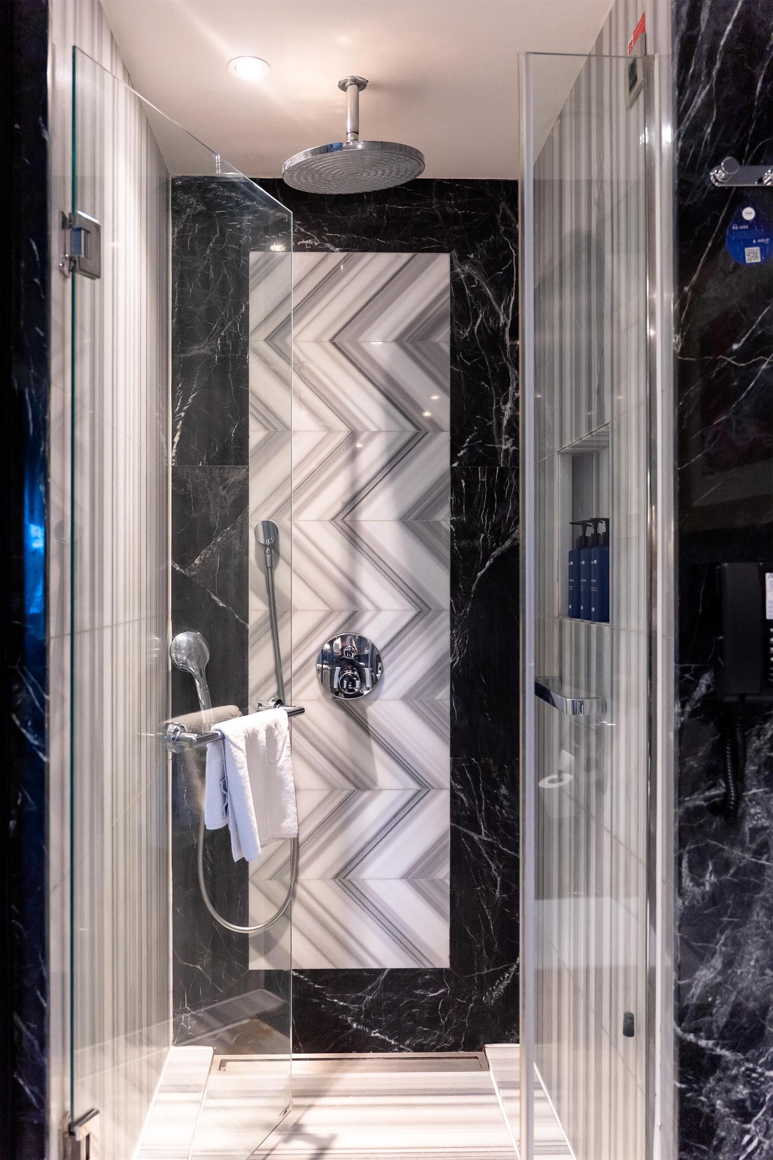 A modern shower enclosure with a marble wall and a glass door.