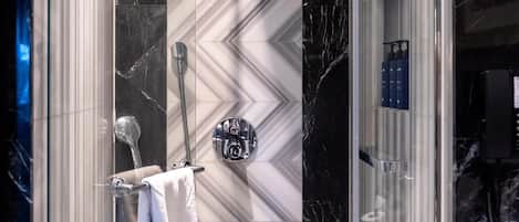 A modern shower enclosure with a marble wall and a glass door.