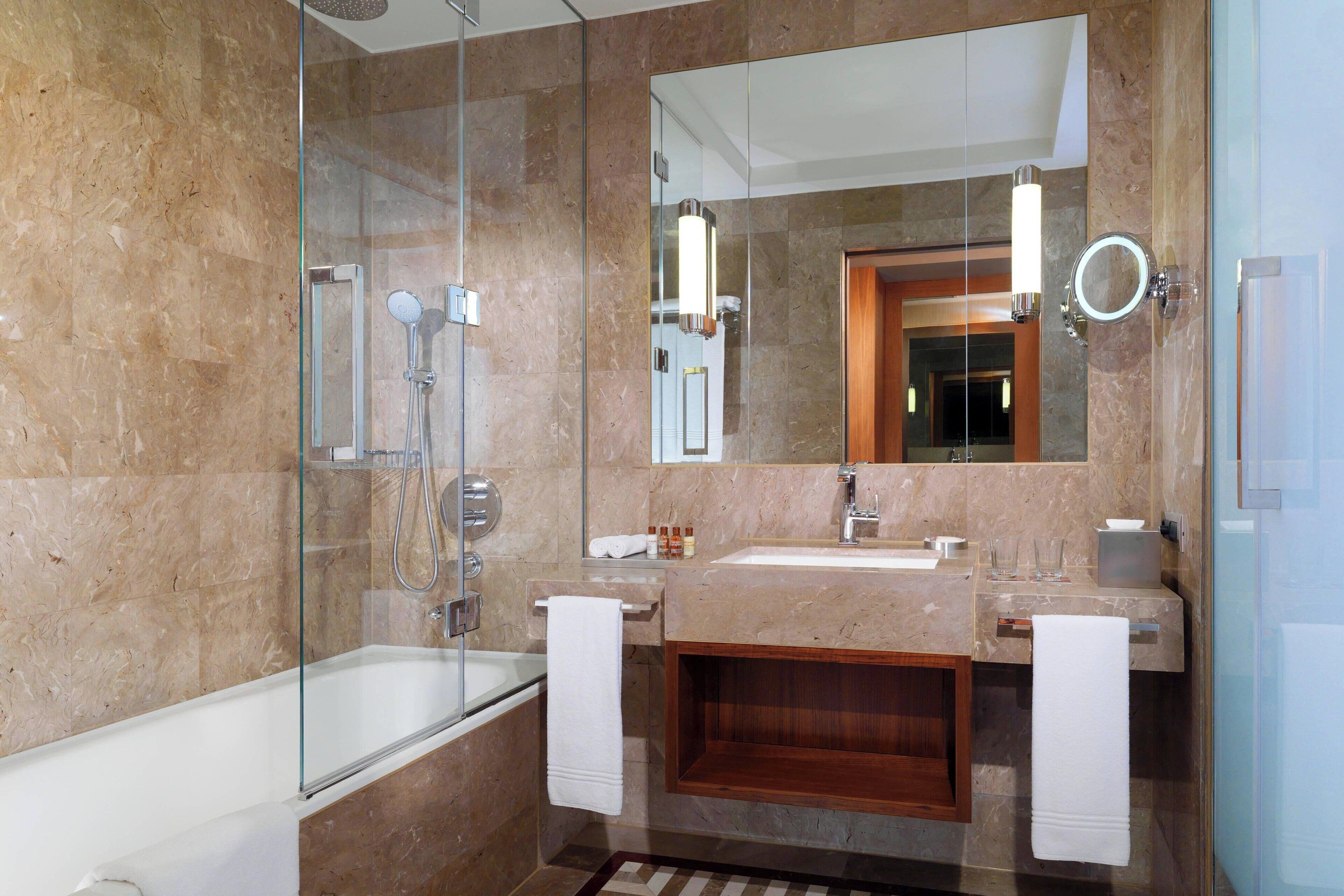A modern bathroom with a glass-enclosed shower, a bathtub, a vanity with a mirror, and a sink.