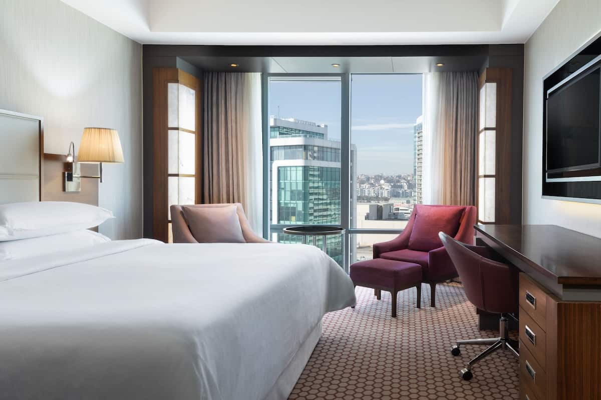 A hotel room with a large bed, two armchairs, a desk, and a TV.