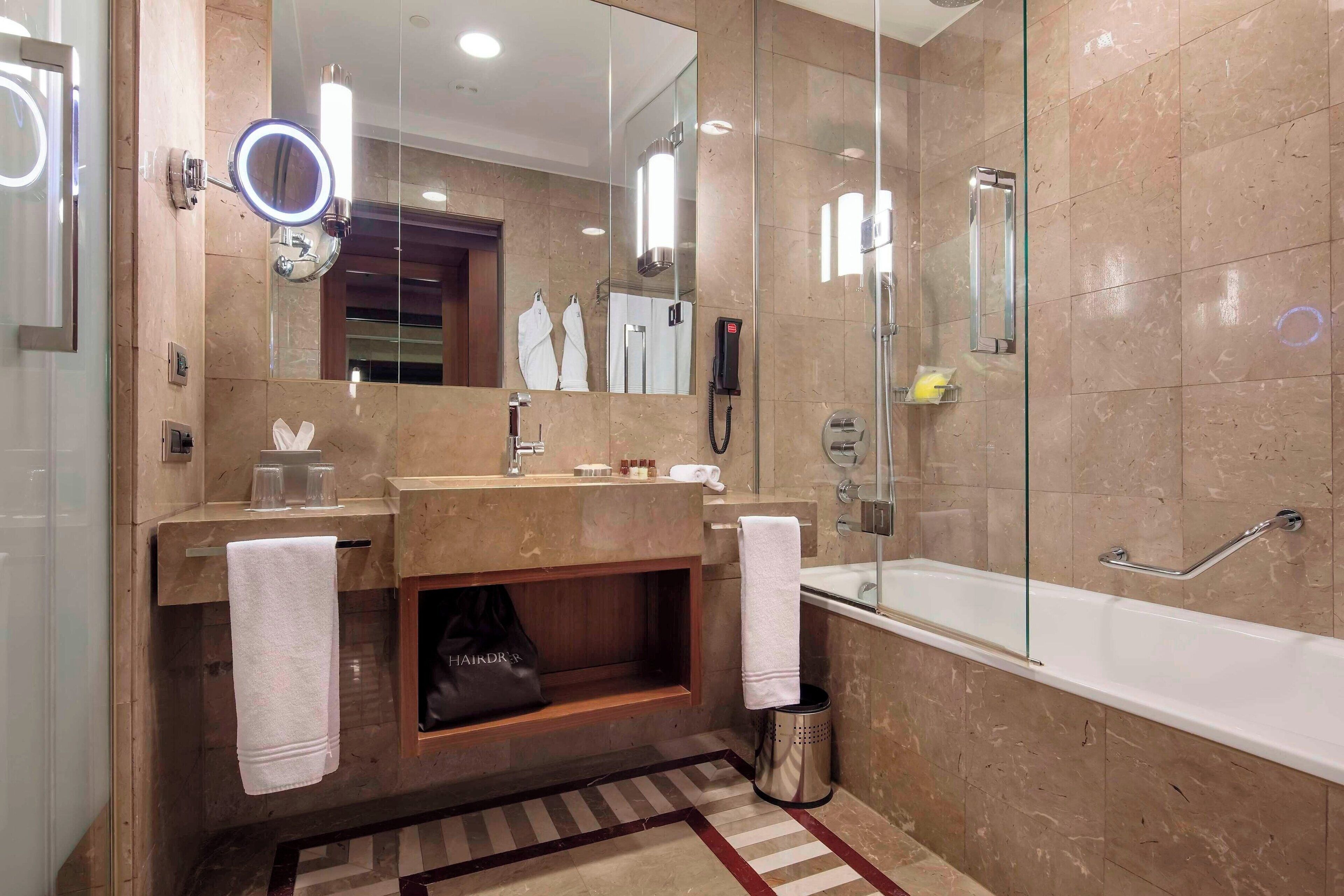 A modern bathroom with a large mirror, a vanity with a sink, a bathtub, and a glass shower enclosure.