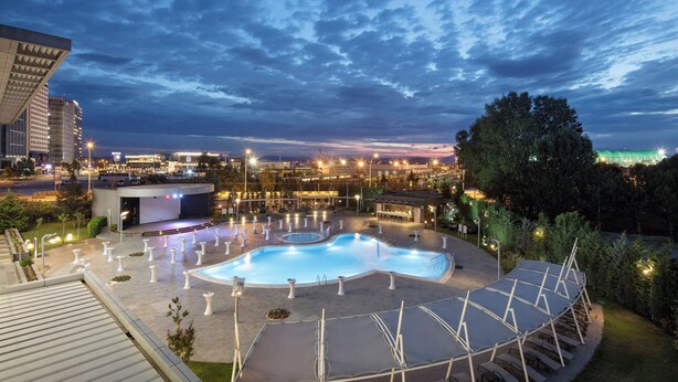 A swimming pool area with a sun deck, surrounded by trees and modern buildings. - Sheraton Bursa Hotel (Bursa)