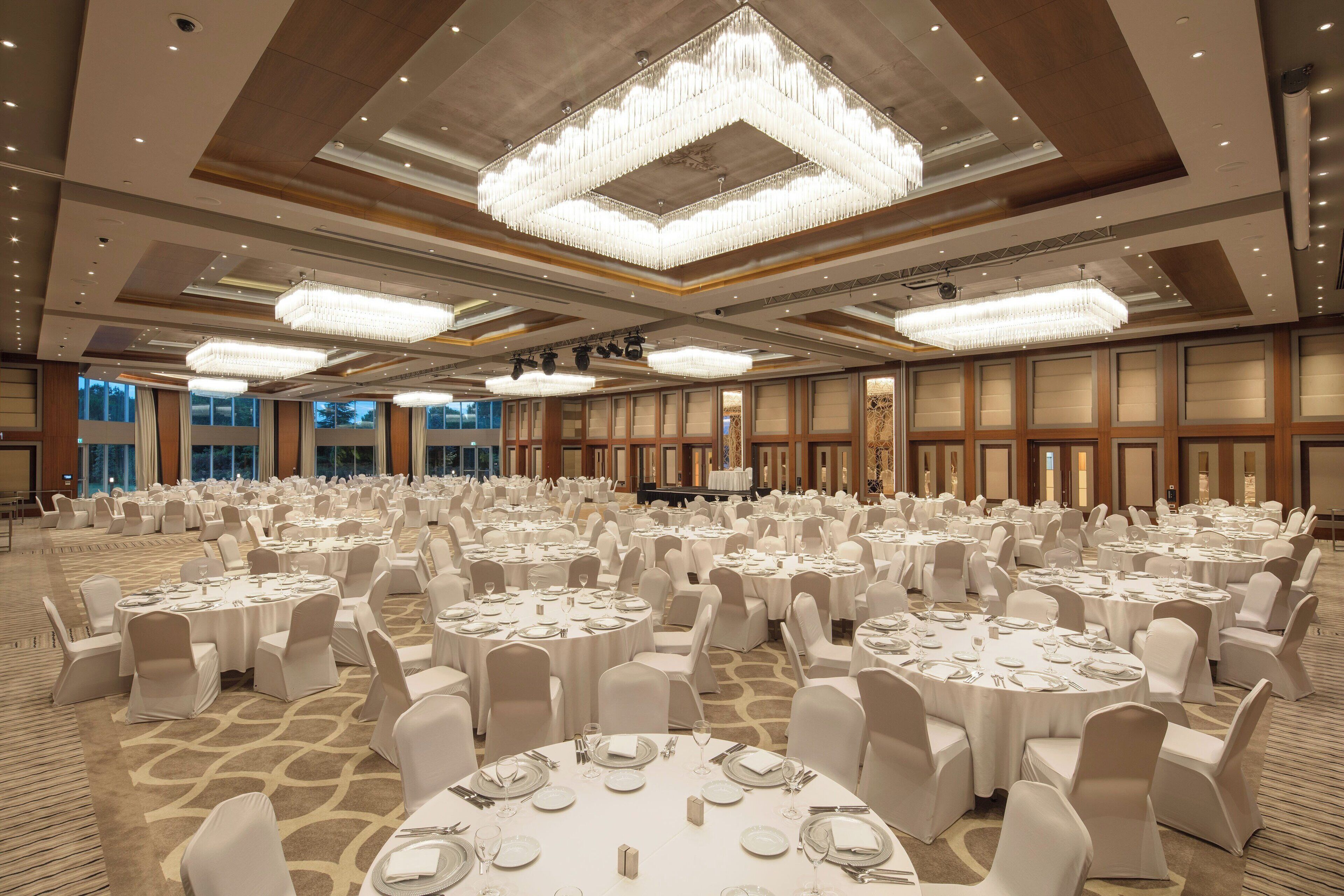 Un gran salón de banquetes con mesas redondas, sillas blancas y candelabros.