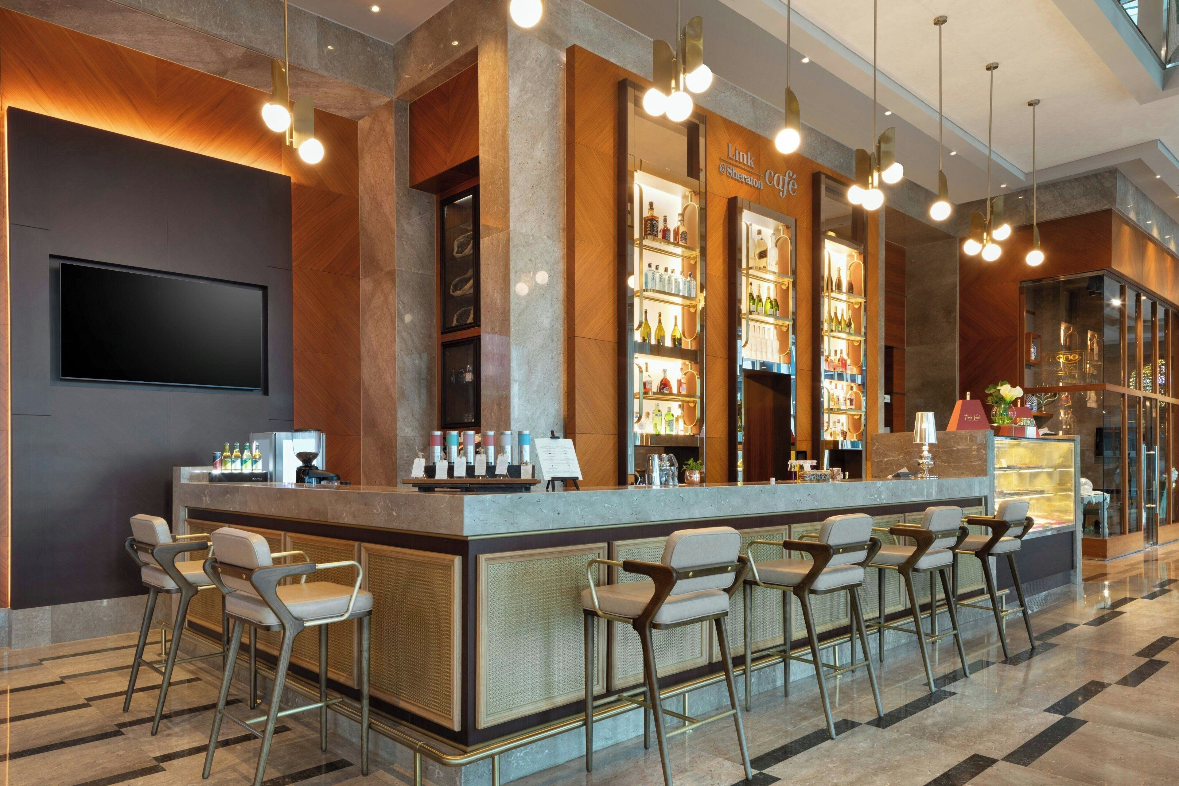 Una zona de bar moderna con encimera de mármol, taburetes y una variedad de botellas y vasos.
