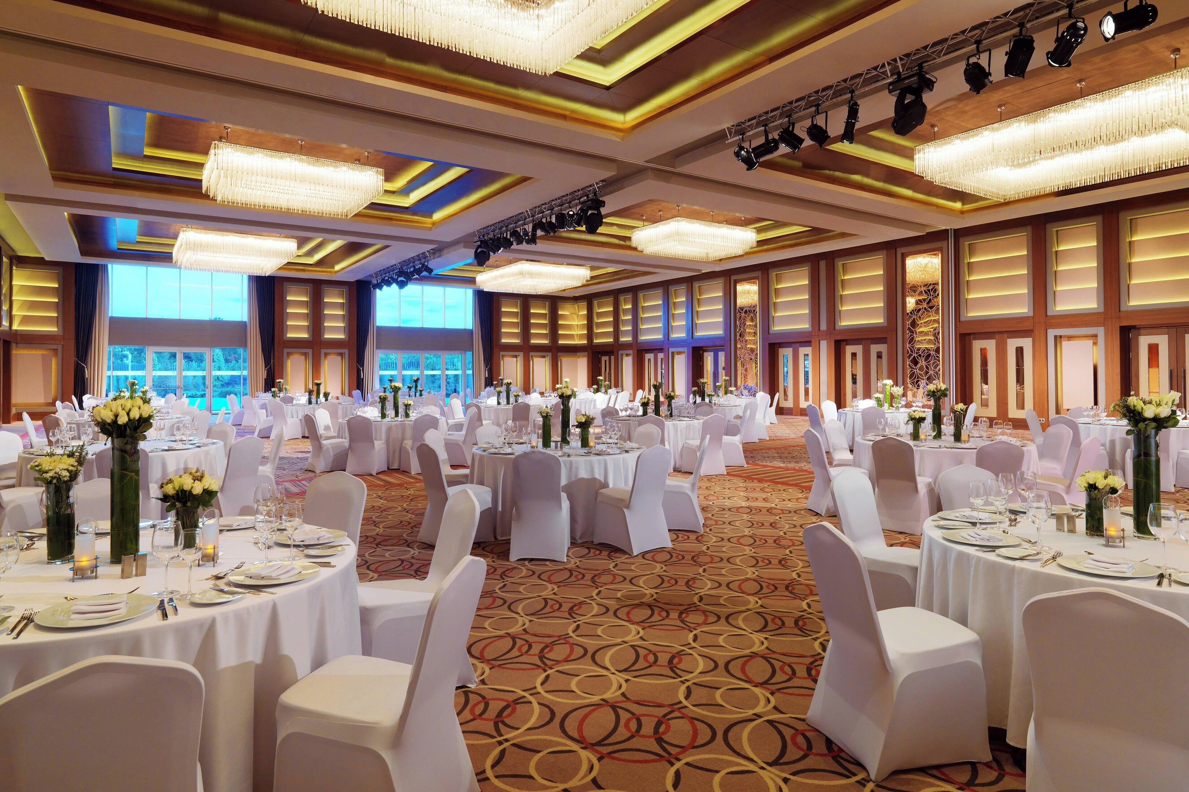 Un salón de banquetes con mesas redondas, sillas blancas y candelabros.