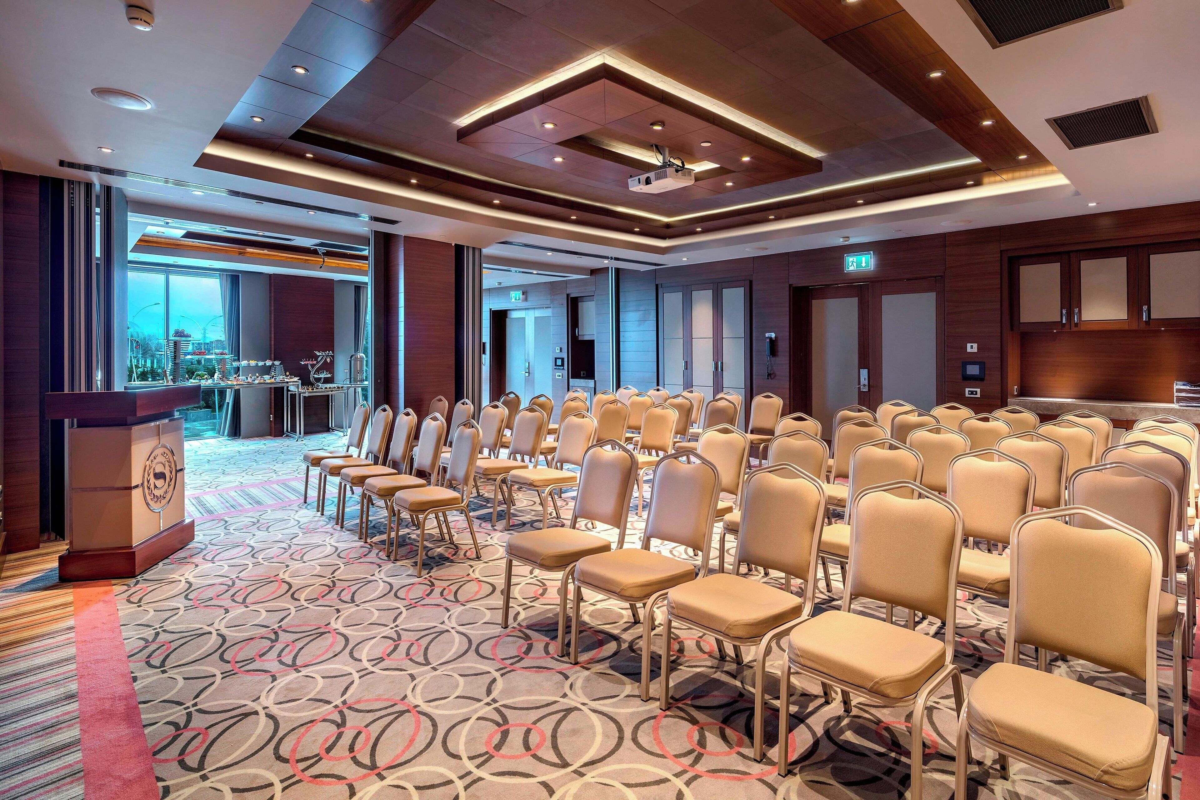 Un salón de conferencias con filas de sillas, un atril y una alfombra estampada.