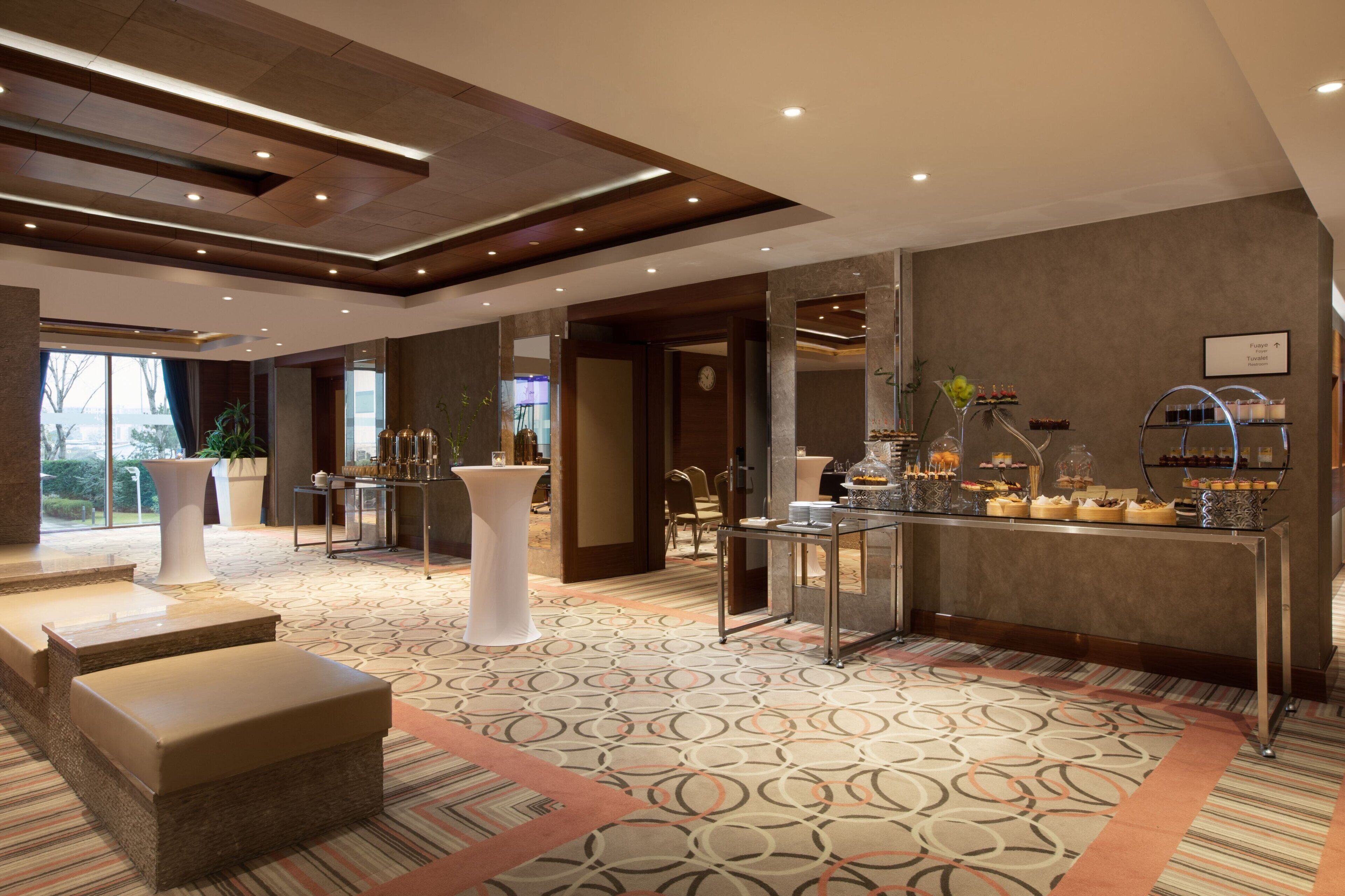 Un moderno vestíbulo de hotel con mostrador de recepción, zona de estar y un bufé con diversas opciones de comida.