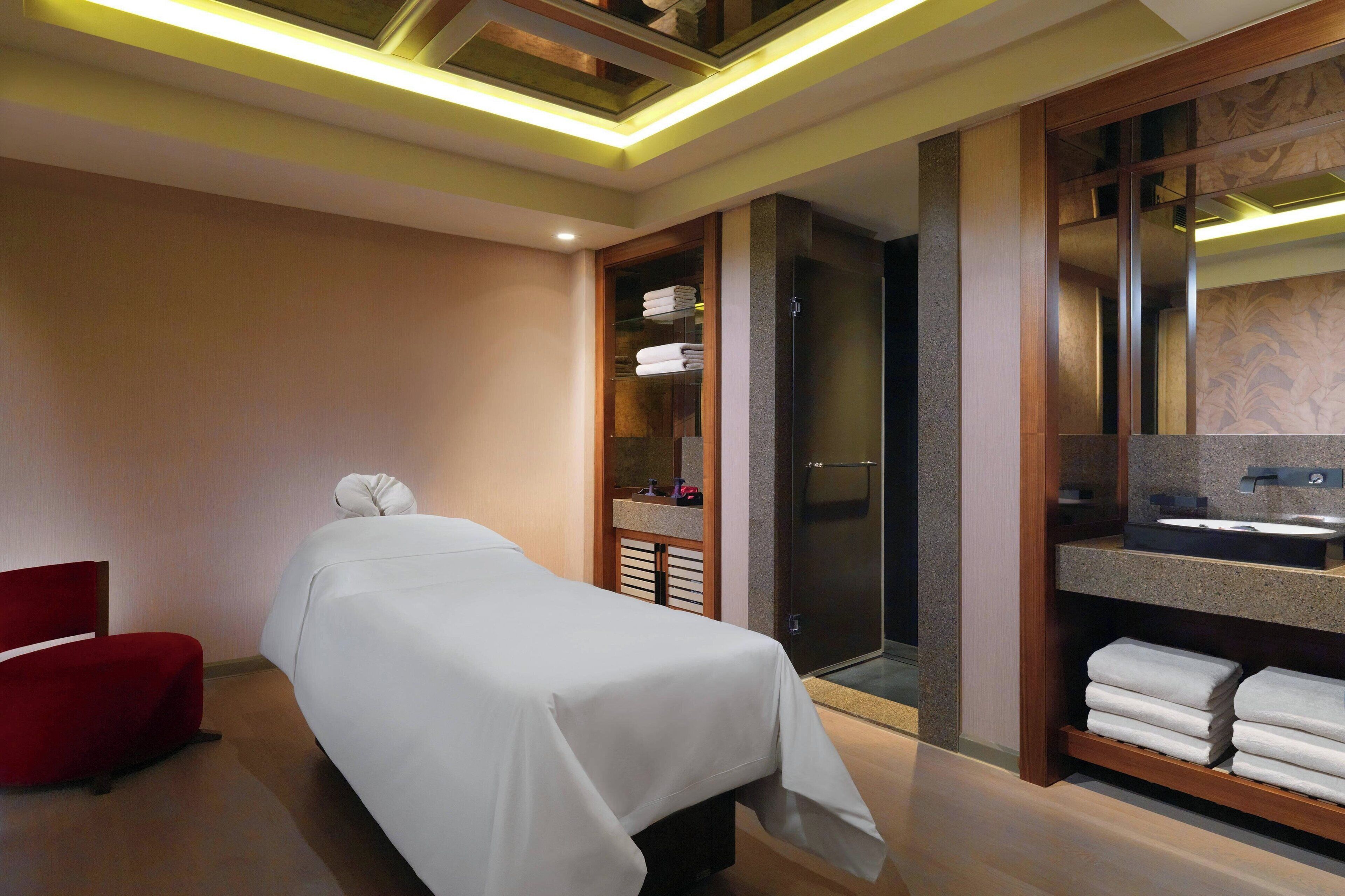 A hotel room with a bed, a red chair, a walk-in closet with towels, a bathroom with a sink, and a shower.