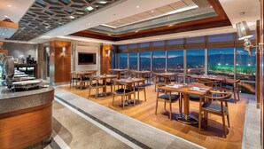 A modern restaurant with a high ceiling, large windows, and a view of a stadium at night. - Sheraton Bursa Hotel (Bursa)