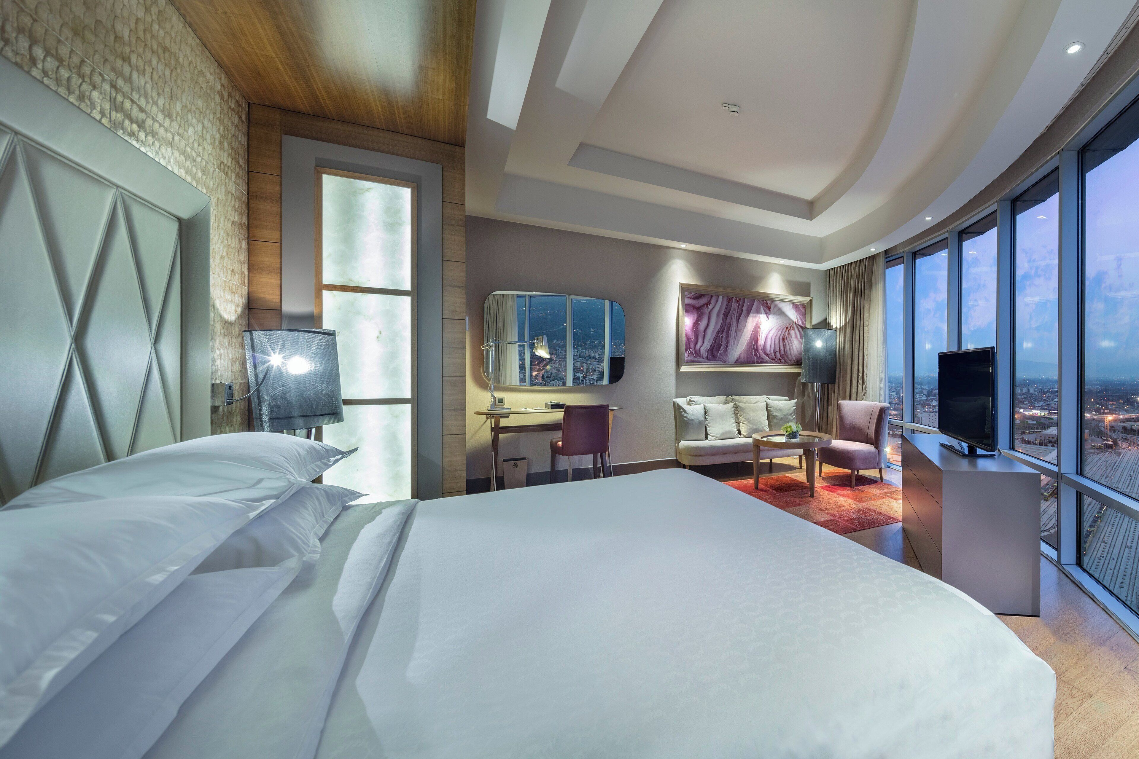A modern hotel room with a large bed, a desk, a sofa, and a TV.