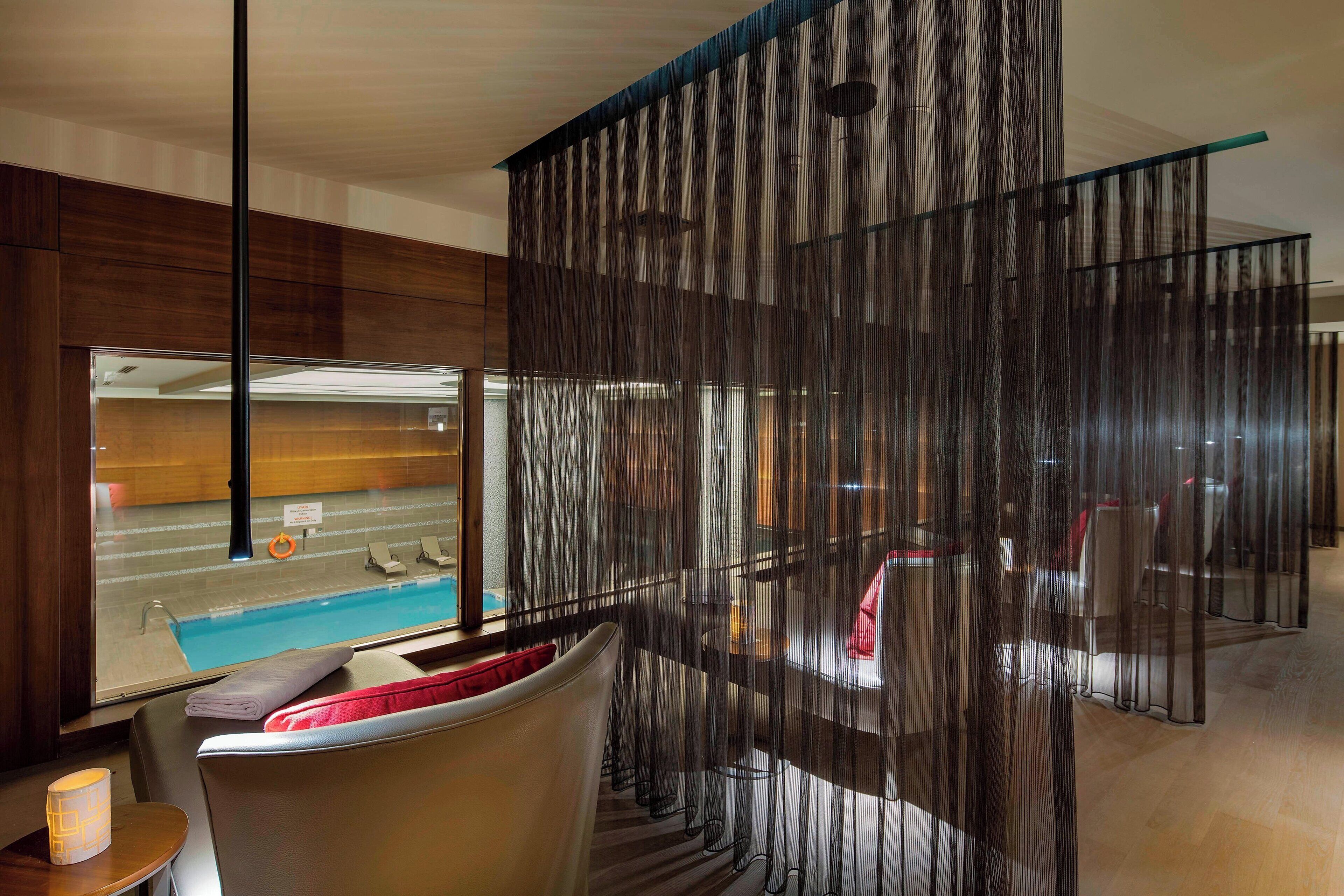 Une chambre d’hôtel moderne dotée d’une grande fenêtre donnant sur une piscine, d’un coin salon avec une table et d’un paravent décoratif.