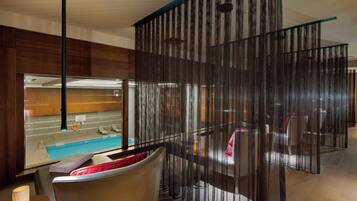 Une chambre d’hôtel moderne dotée d’une grande fenêtre donnant sur une piscine, d’un coin salon avec une table et d’un paravent décoratif.