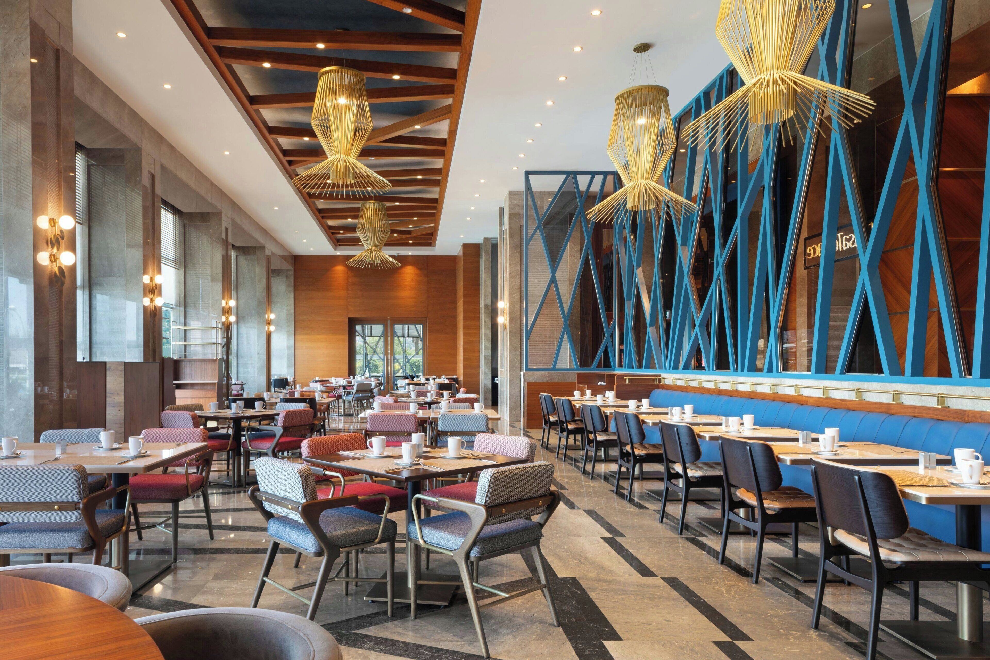 A spacious dining area with multiple tables and chairs, large windows, and modern lighting fixtures.