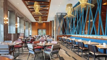 A spacious dining area with multiple tables and chairs, large windows, and modern lighting fixtures.