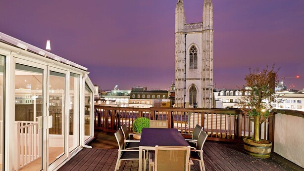 Terraza en la azotea con una mesa y sillas, con vistas a una torre de una iglesia histórica.