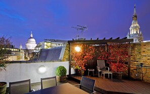 An outdoor patio with a brick wall, red foliage, and a table with chairs. - Cheval Calico House (London)