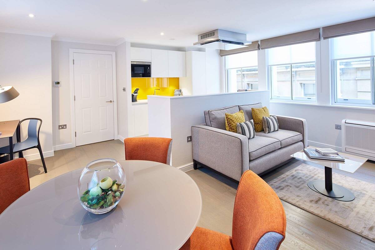 Un appartement moderne comprenant un coin repas, un salon avec un canapé et des coussins, et une cuisine agrémentée d’un mur d’accent jaune.