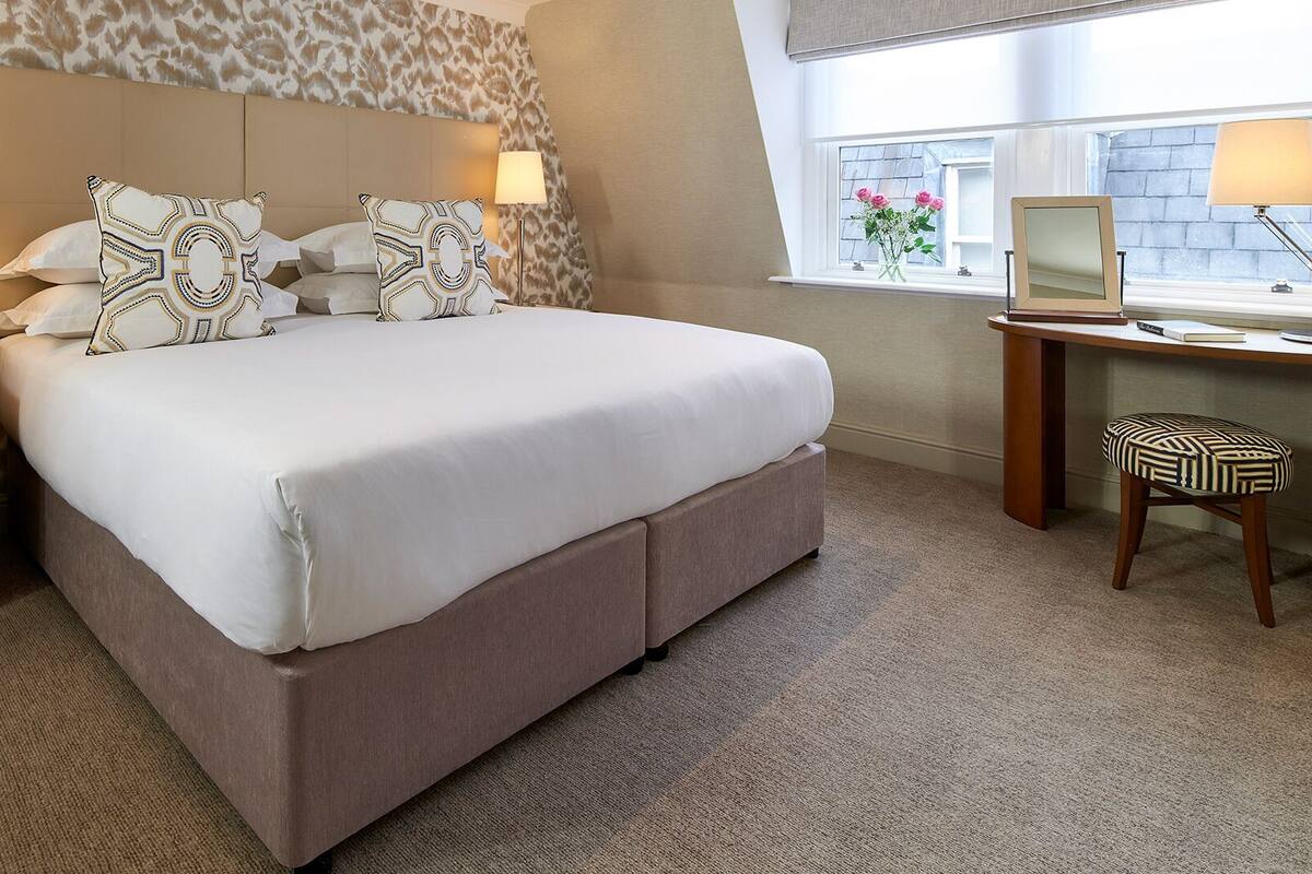 Une chambre d’hôtel avec un grand lit, des lampes de chevet, un bureau avec une chaise et une fenêtre décorée de fleurs.