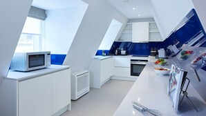 Una cocina moderna con armarios blancos, microondas integrado, cafetera y frutero sobre la encimera.