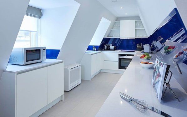 A modern kitchen with white cabinetry, a built-in microwave, a coffee machine, and a fruit bowl on the counter. - Cheval Calico House (London)