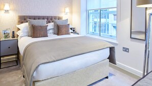 Un dormitorio ordenado con una cama grande, dos mesitas de noche, una lámpara de pared y una ventana con vistas.